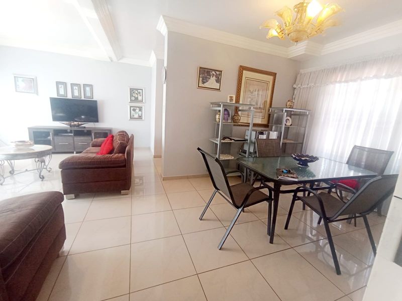 An open-plan living and dining area featuring neutral tiled flooring, decorative ceiling cornices, and a central chandelier, providing a functional and connected living space.