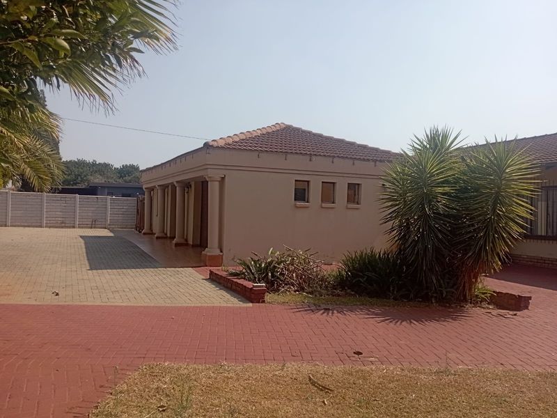 Rear view of the property featuring a paved driveway, covered patio area with columns, and a tiled roof structure.