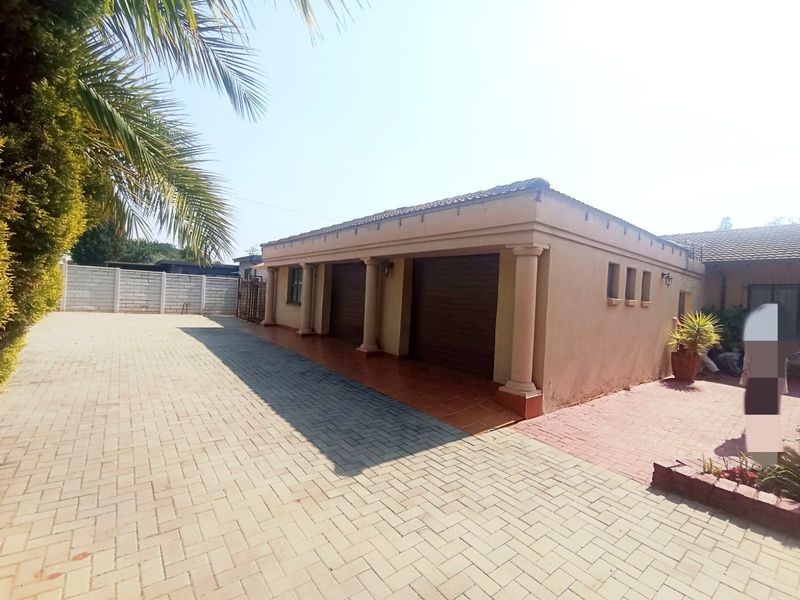 A well-maintained exterior view featuring a double garage with decorative columns and an extensive paved driveway area.