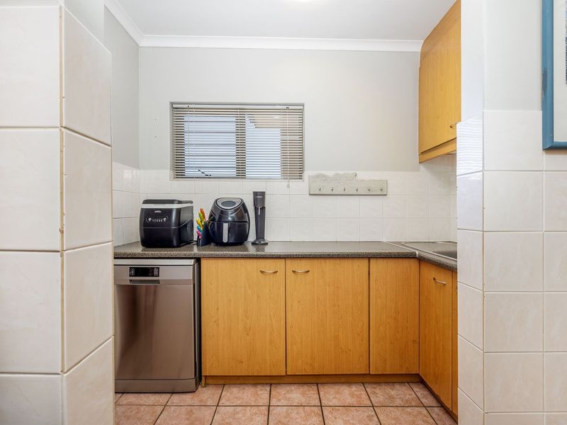 A functional scullery area featuring laminate cabinetry, stone-look countertops, tiled splashbacks, and ceramic floor tiles, providing additional workspace and storage.