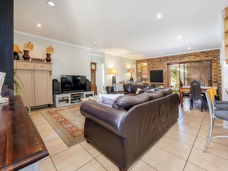 Spacious open-plan living and dining area featuring tiled floors, recessed lighting, and an exposed brick feature wall with access to the outdoor space.