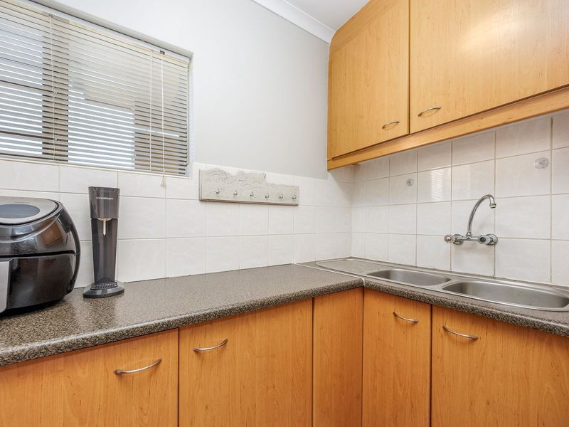 A functional scullery area featuring laminate cabinetry, a double bowl stainless steel sink, and tiled splashbacks, providing practical prep and wash-up space.