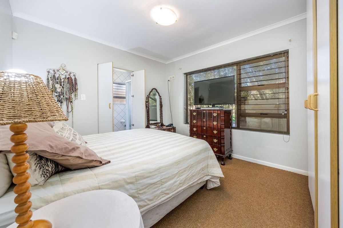 A functional bedroom featuring carpeted flooring, built-in wardrobe storage, and an adjoining en-suite bathroom with natural light through large windows.