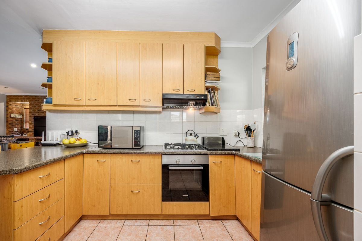 A functional kitchen featuring light wood cabinetry, laminate countertops, a tiled backsplash, and integrated appliances including an oven and gas hob.