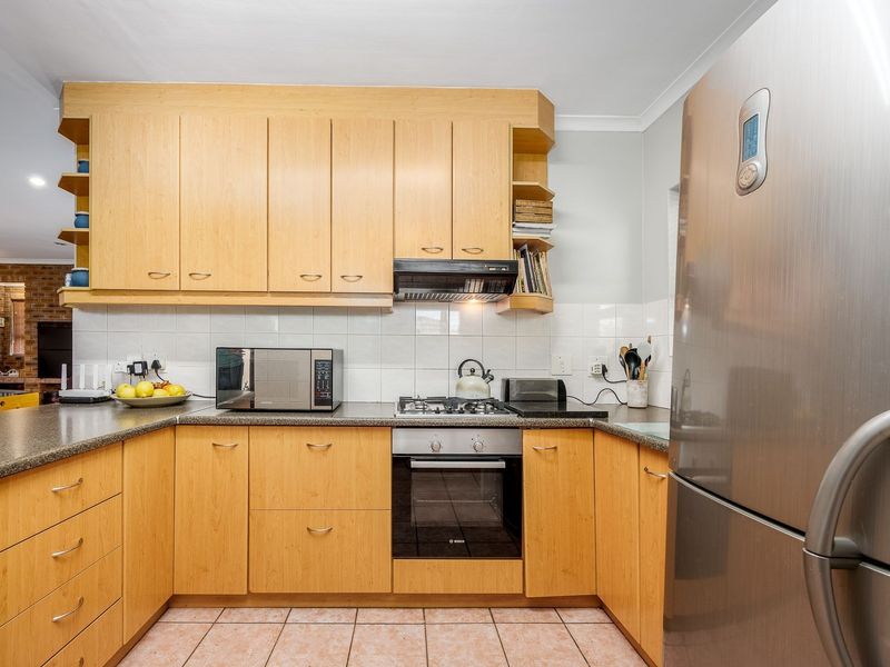 A functional kitchen featuring light wood cabinetry, laminate countertops, a tiled backsplash, and integrated appliances including an oven and gas hob.