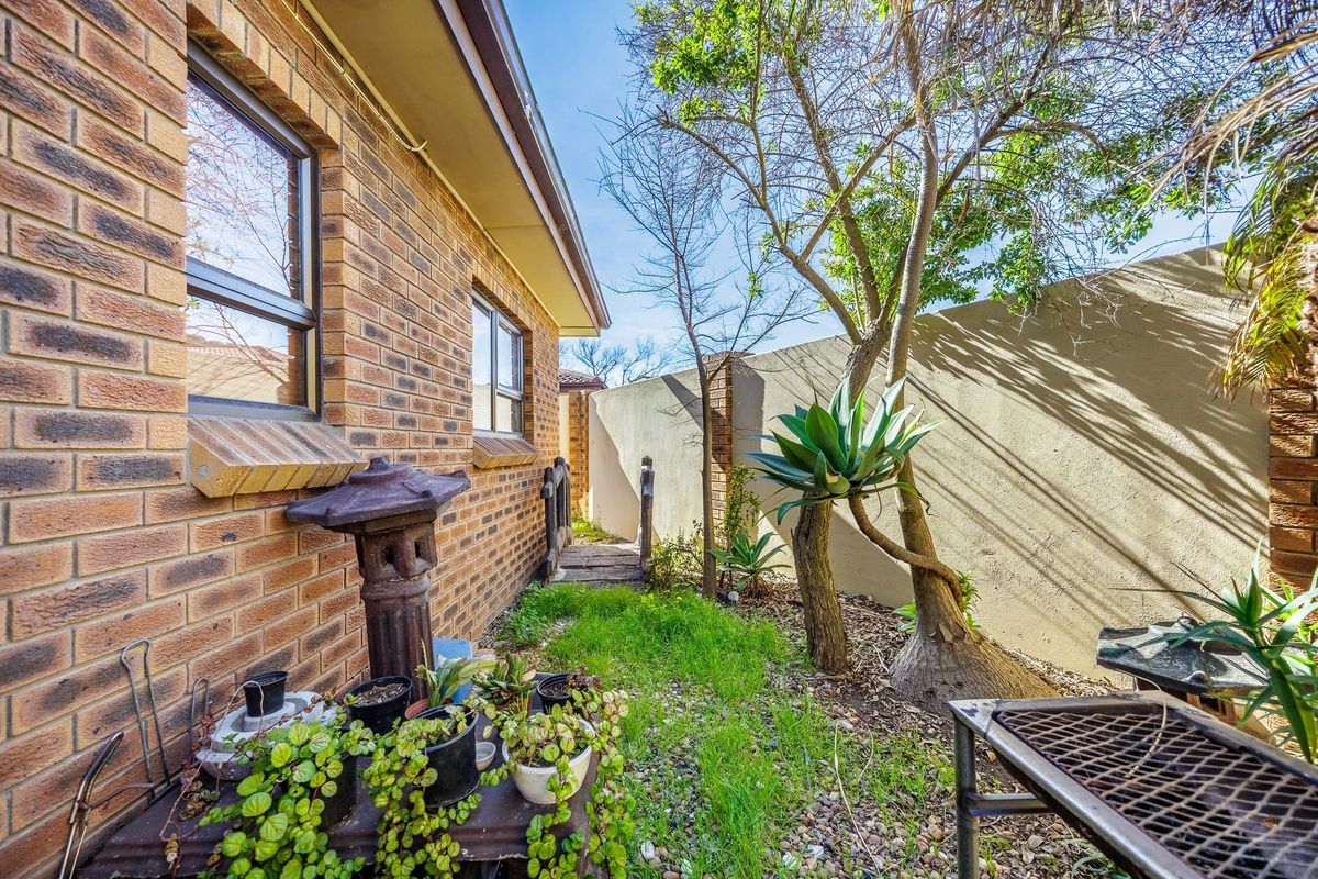 A side garden area featuring a brick townhouse facade, boundary wall, and established trees, providing a private outdoor space.