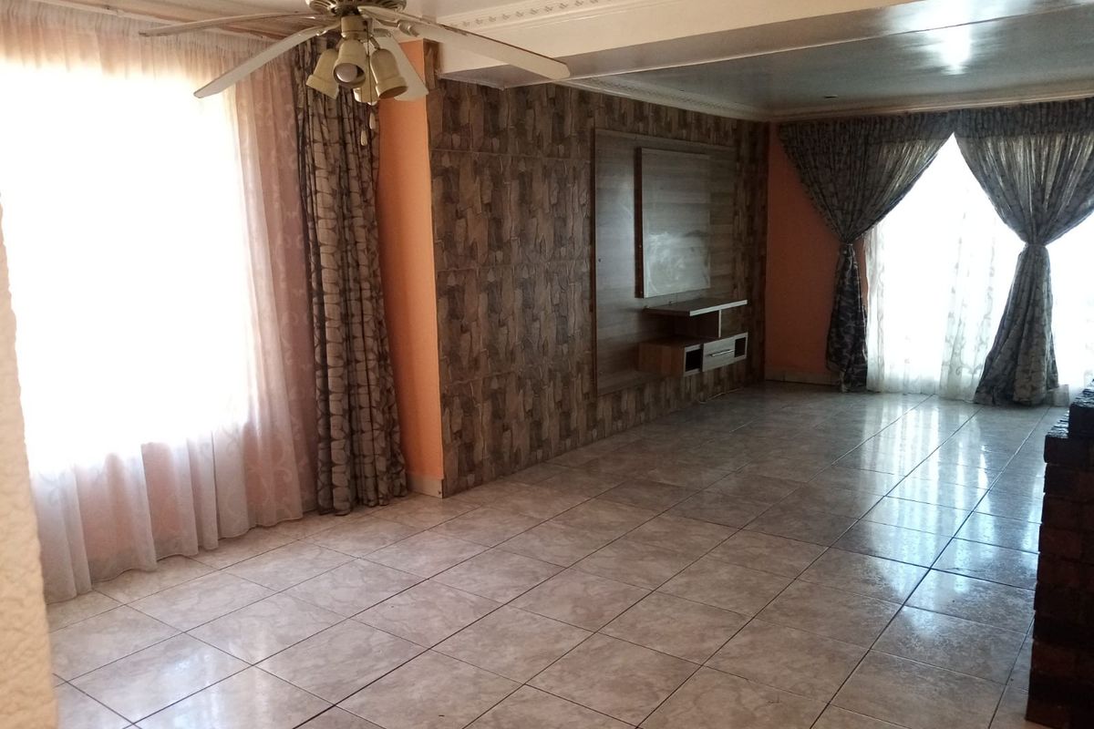 Spacious living room featuring tiled flooring, a built-in media console, decorative wall cladding, and a ceiling fan.