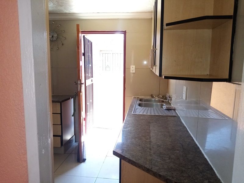 A functional kitchen area featuring built-in cabinetry, laminate countertops, a double stainless steel sink, and direct access to the exterior via a security gate.