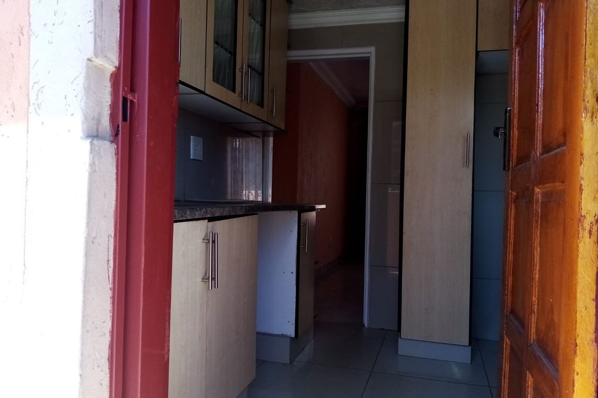 A compact kitchen featuring built-in cabinetry, laminate countertops, and tiled flooring, viewed from an adjacent doorway.