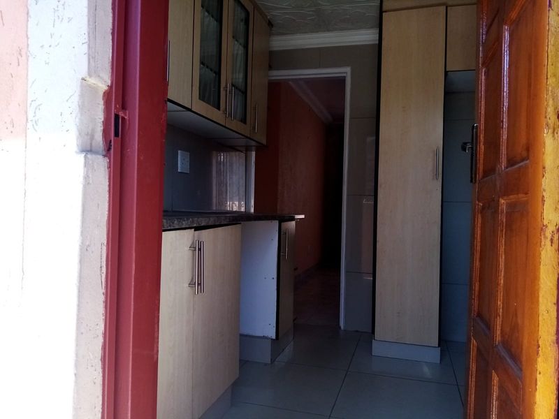 A compact kitchen featuring built-in cabinetry, laminate countertops, and tiled flooring, viewed from an adjacent doorway.
