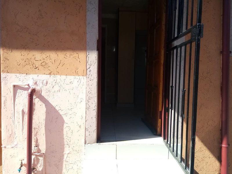 An exterior view of the property entrance featuring a security gate, tiled threshold, and textured wall finish with an external water tap.