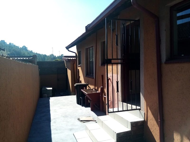 A rear exterior view showing a concrete paved area, tiled steps leading to a security gate, and a boundary wall.