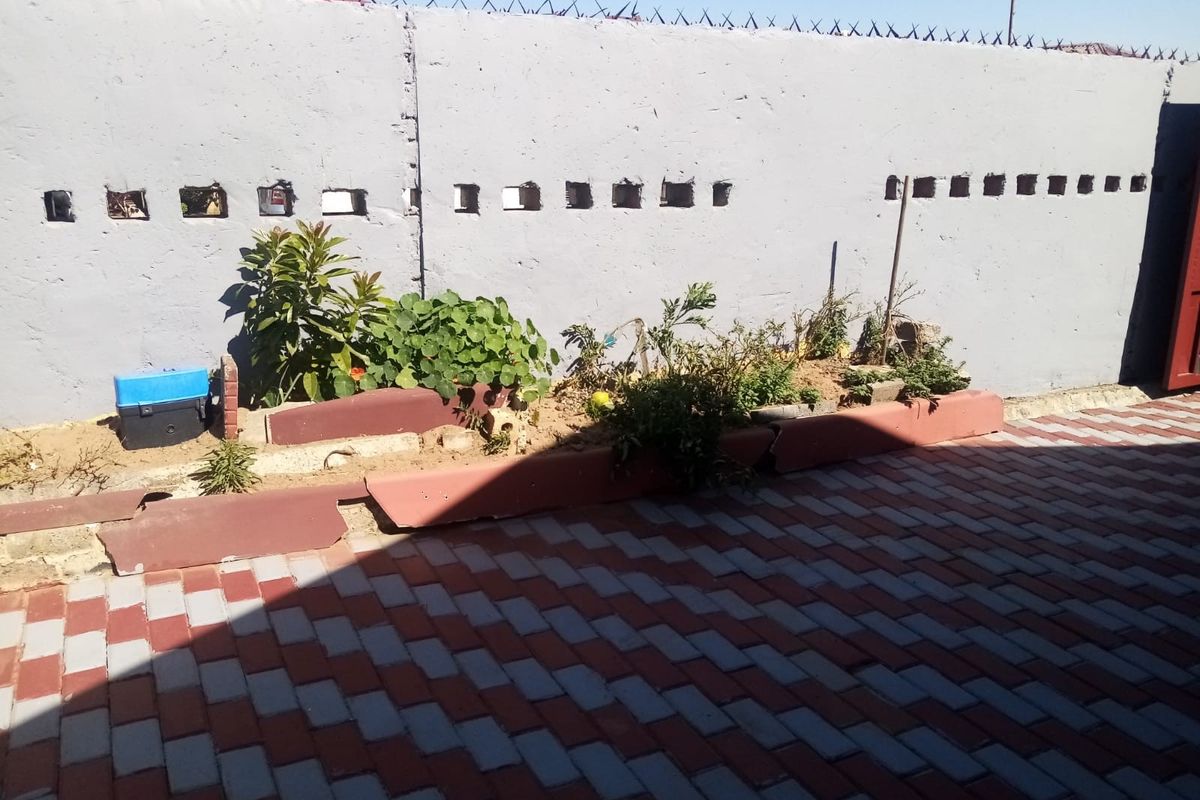 A rear exterior area featuring a paved surface, a raised garden bed, and a perimeter wall secured with razor wire.