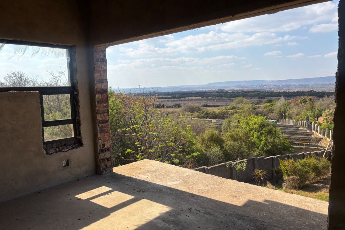 An unfinished interior space featuring exposed brickwork and concrete flooring, offering expansive elevated views of the surrounding landscape.