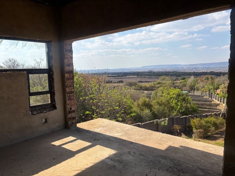 An unfinished interior space featuring exposed brickwork and concrete flooring, offering expansive elevated views of the surrounding landscape.