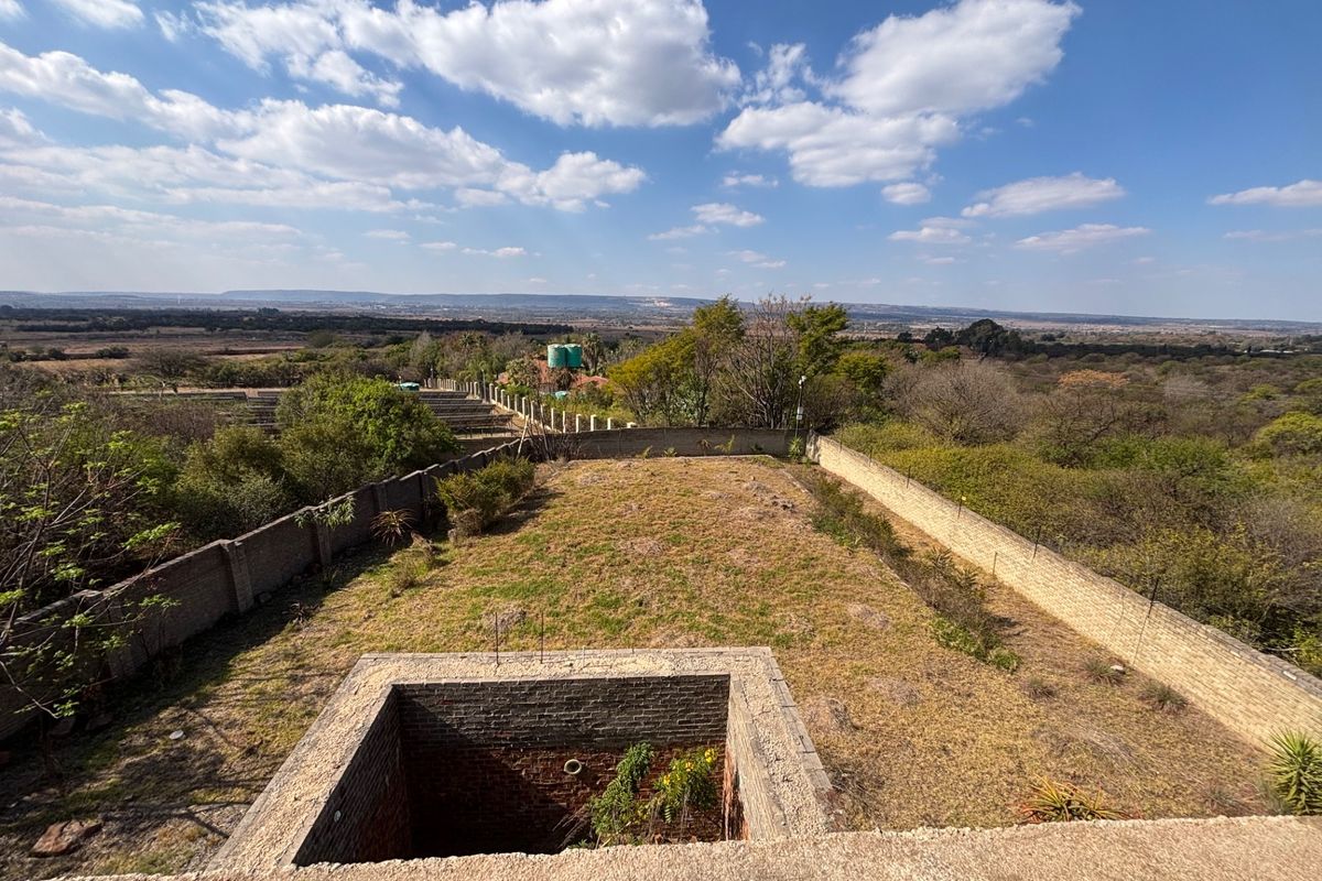 An elevated view of a large plot featuring a perimeter brick wall, an unfinished sunken brick structure, and expansive surrounding landscape.