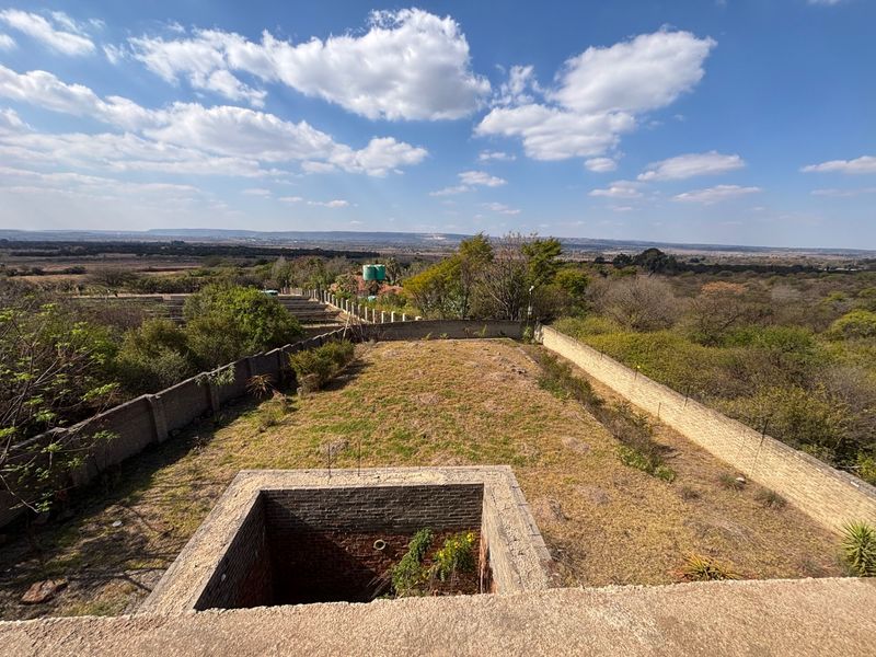 An elevated view of a large plot featuring a perimeter brick wall, an unfinished sunken brick structure, and expansive surrounding landscape.
