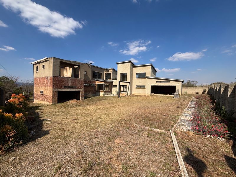 Rear view of a large residential property currently under construction, featuring exposed brick and plaster finishes with an expansive, unlandscaped backyard area.
