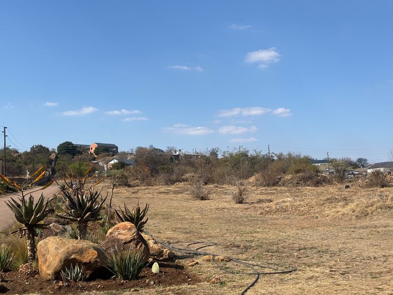 A view of a vacant plot of land with a landscaped rock garden in the foreground and surrounding residential neighborhood in the distance.