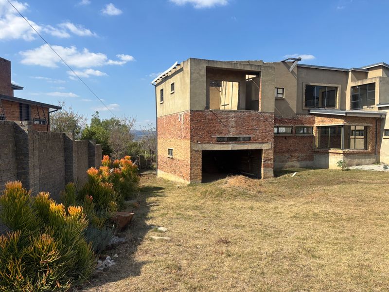 Rear view of a residential property under construction, featuring exposed brickwork, unfinished structural elements, and a large backyard area.