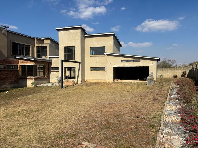 Rear view of a double-storey house under construction, featuring an open garage, unfinished exterior walls, and a large, unlandscaped garden area.