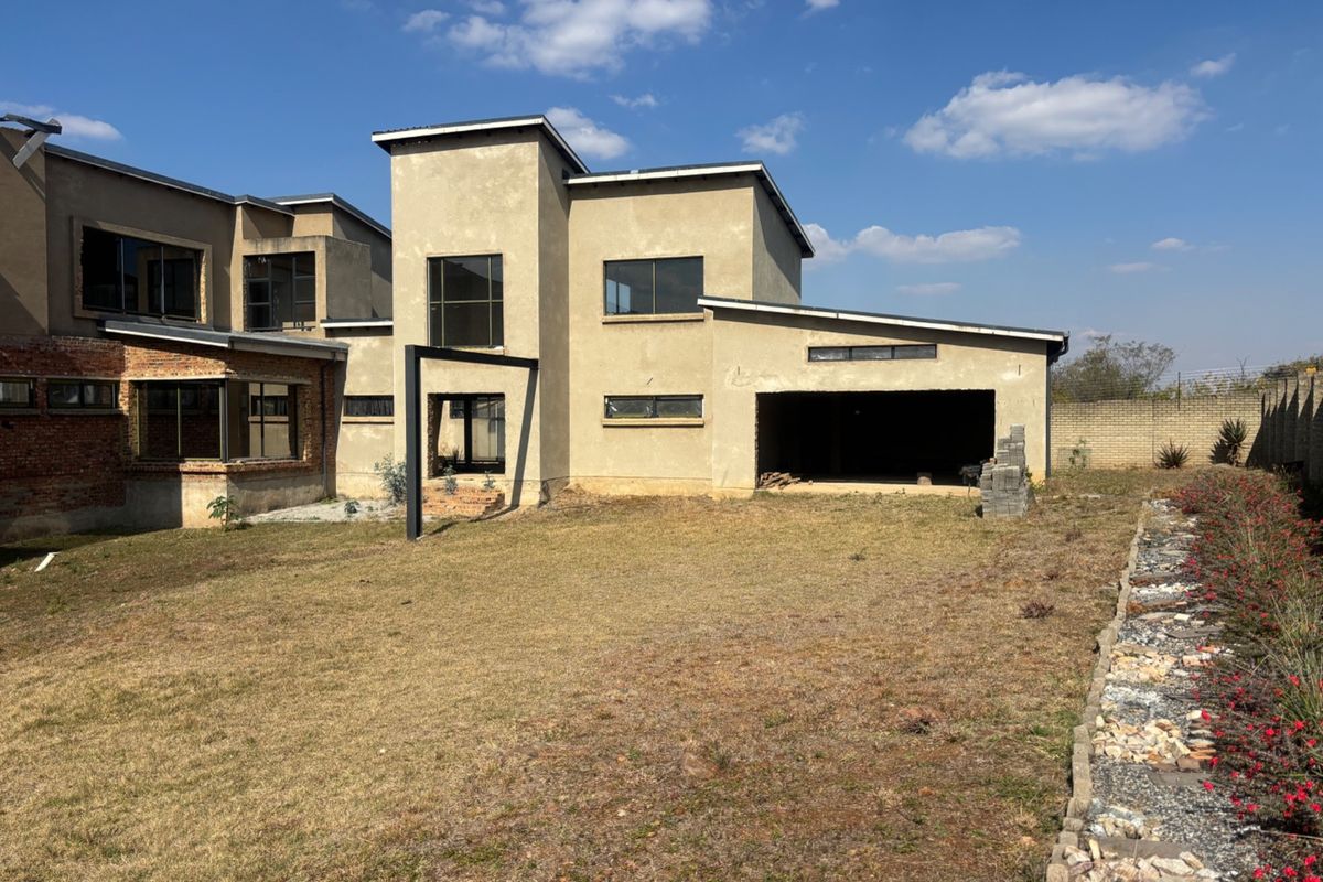 Rear view of a double-storey house under construction, featuring an open garage, unfinished exterior walls, and a large, unlandscaped garden area.