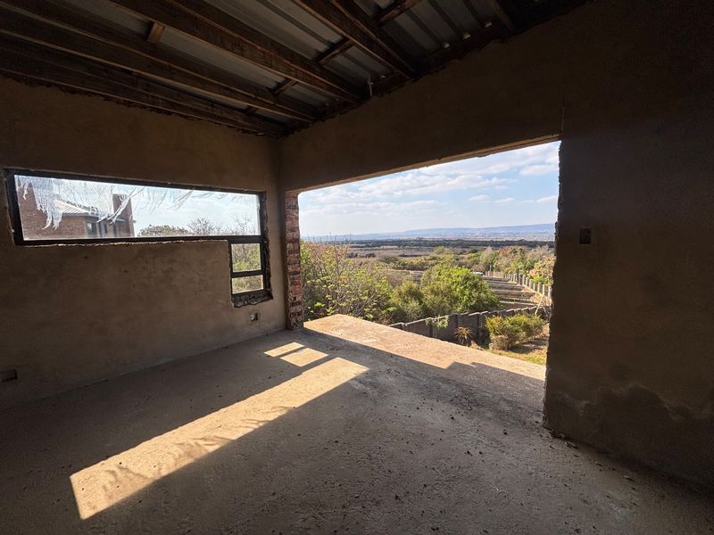 An unfinished interior space featuring exposed timber roof beams, concrete flooring, and a large open aperture offering expansive views of the surrounding landscape.