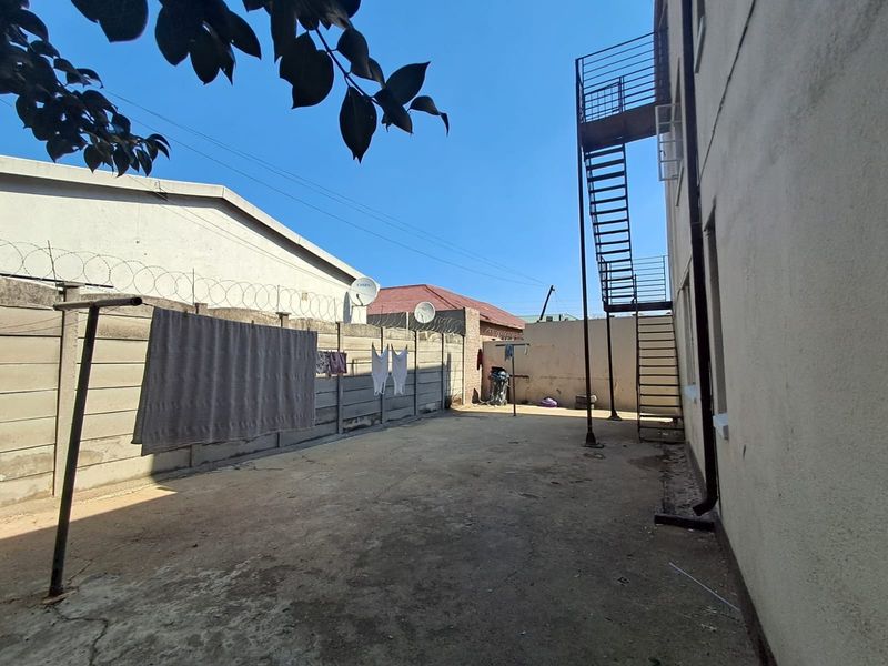 Rear exterior area featuring concrete paving, perimeter wall with razor wire security, and an external metal staircase providing access to the upper level.
