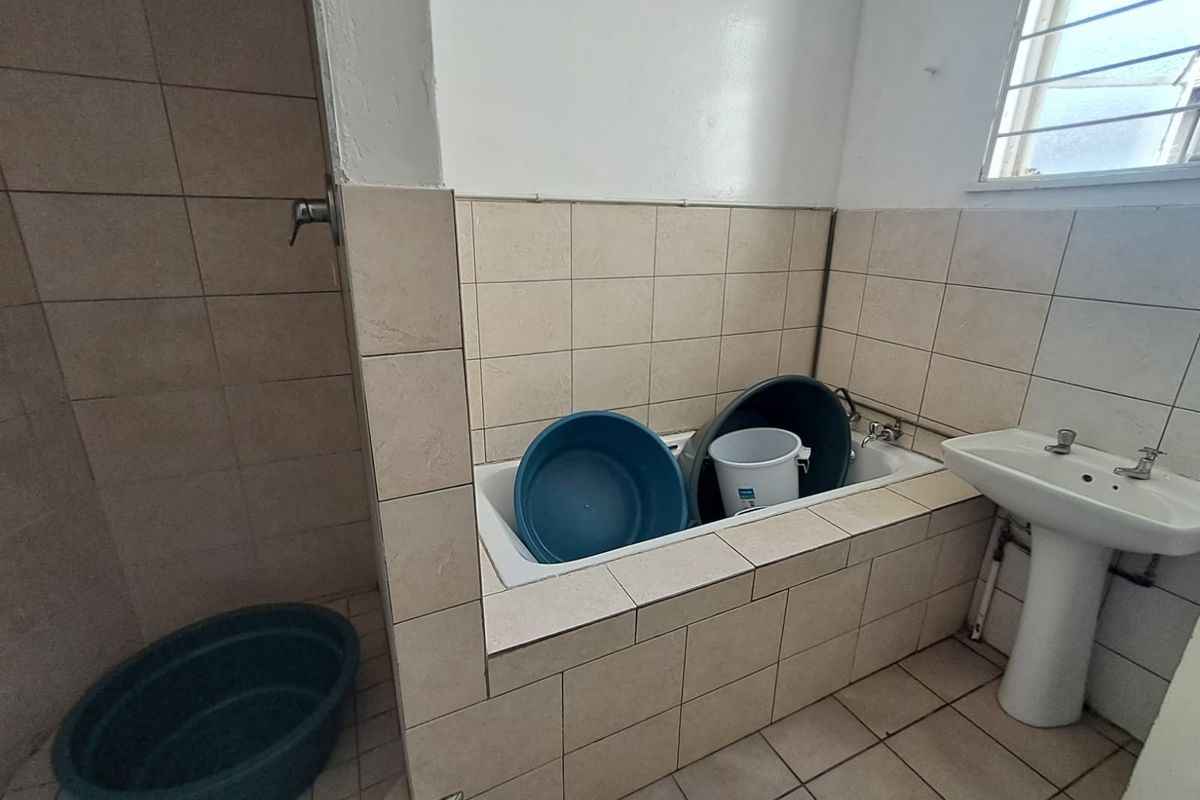 A functional bathroom featuring a tiled bathtub, pedestal basin, and shower area, requiring cosmetic updates to improve its overall condition and aesthetic appeal.