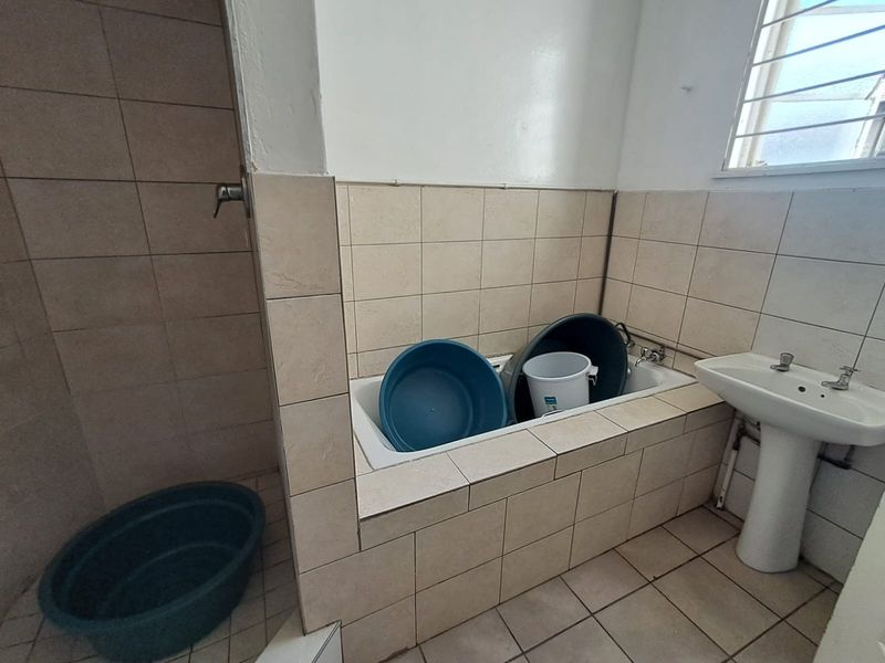 A functional bathroom featuring a tiled bathtub, pedestal basin, and shower area, requiring cosmetic updates to improve its overall condition and aesthetic appeal.