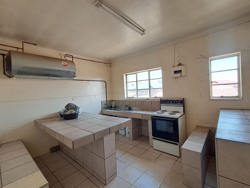 A dated kitchen featuring tiled countertops, a freestanding stove, and a stainless steel sink, requiring renovation to modernize the space.