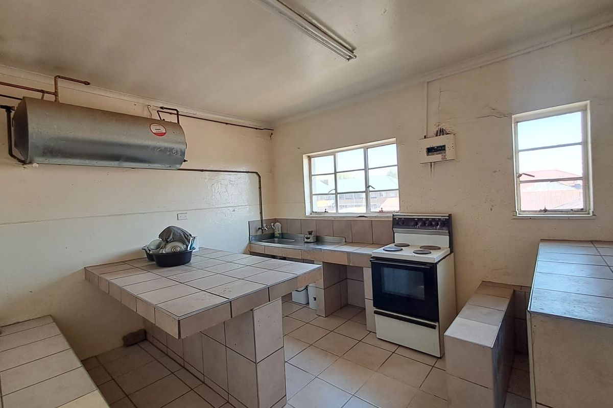 A dated kitchen featuring tiled countertops, a freestanding stove, and a stainless steel sink, requiring renovation to modernize the space.