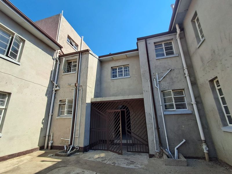 Rear exterior view of the property featuring a security gate, multiple casement windows, and exposed plumbing infrastructure against a weathered plaster facade.