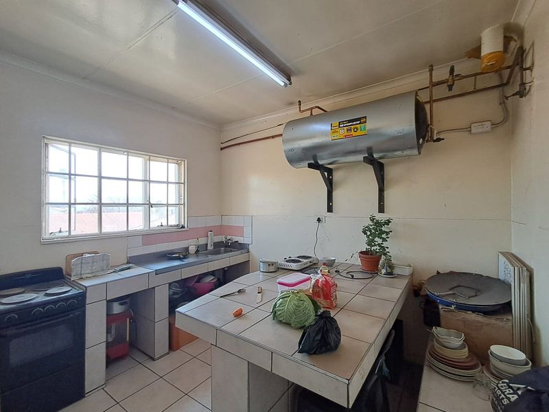A functional kitchen featuring tiled countertops, a stainless steel sink, and an exposed electric geyser, requiring cosmetic updates to modernize the space.