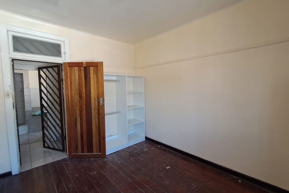 An empty bedroom featuring original timber flooring, a picture rail, and a security gate leading to an adjacent room.