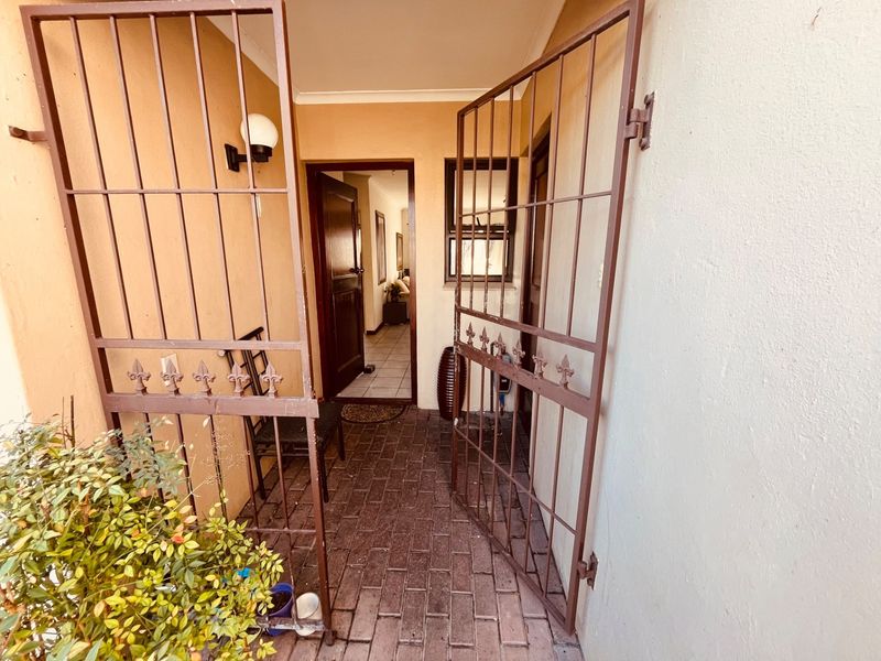 A secure entrance area featuring a metal security gate, brick paved flooring, and a timber front door leading into the home.
