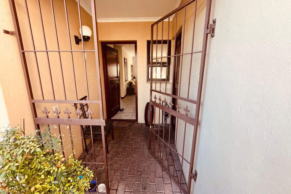 A secure entrance area featuring a metal security gate, brick paved flooring, and a timber front door leading into the home.