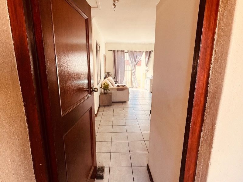 A view through a wooden doorway into a tiled hallway leading towards a living area with access to an outdoor space.