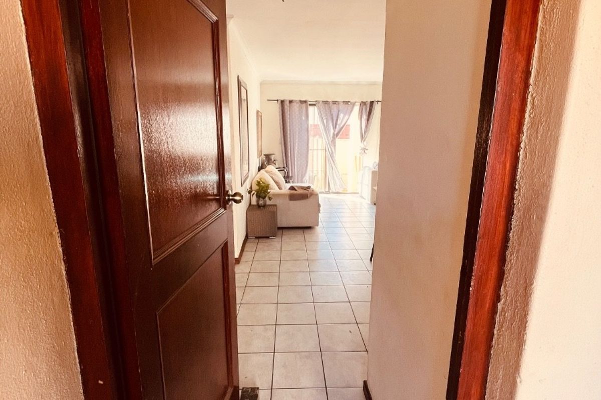 A view through a wooden doorway into a tiled hallway leading towards a living area with access to an outdoor space.