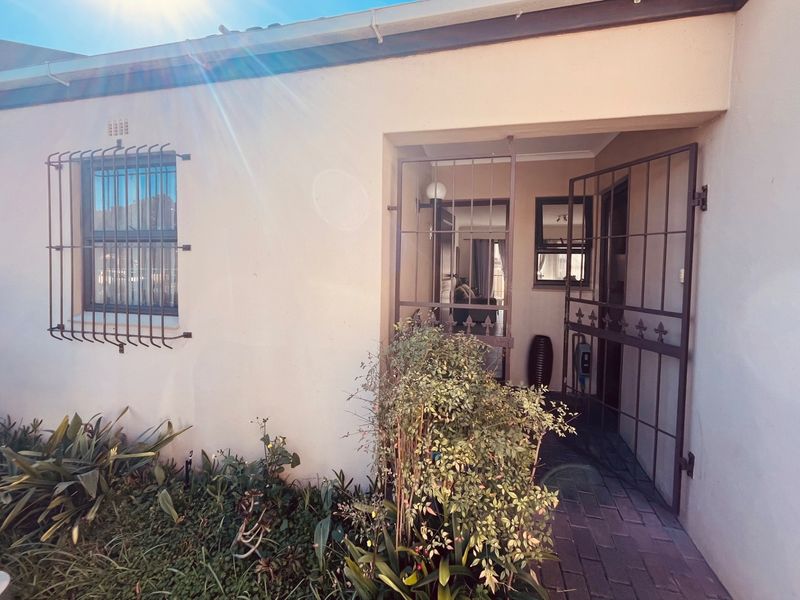 Front entrance of the townhouse featuring a security gate, paved walkway, and security bars on the window.