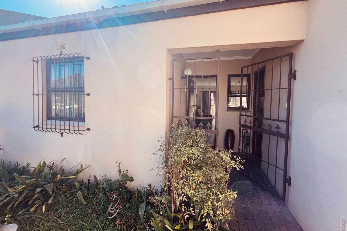 Front entrance of the townhouse featuring a security gate, paved walkway, and security bars on the window.