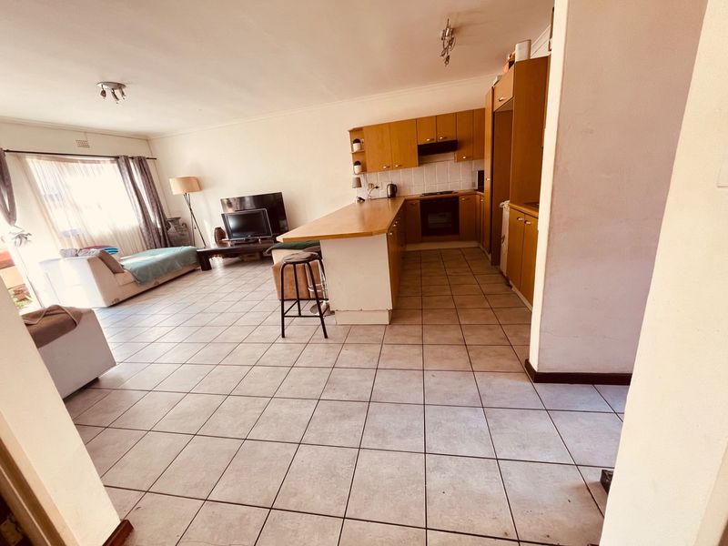 Open-plan living area featuring a functional kitchen with built-in cabinetry, breakfast bar, and tiled flooring throughout the combined space.