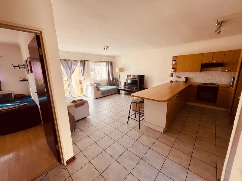Open-plan living area featuring a functional kitchen with built-in cabinetry, breakfast bar, and tiled flooring throughout, leading to a bright lounge space.