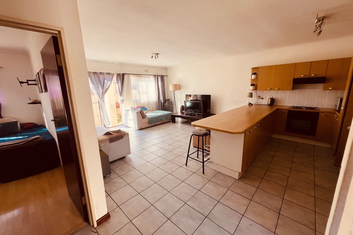 Open-plan living area featuring a functional kitchen with built-in cabinetry, breakfast bar, and tiled flooring throughout, leading to a bright lounge space.