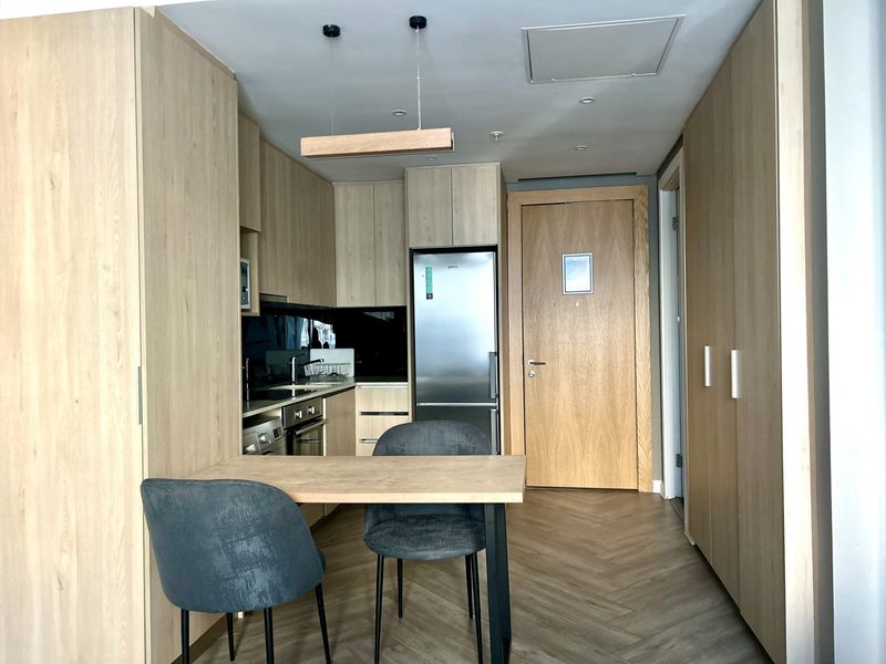 Modern kitchen featuring light wood cabinetry, integrated appliances, herringbone flooring, and a compact dining area, presenting a clean and contemporary aesthetic.