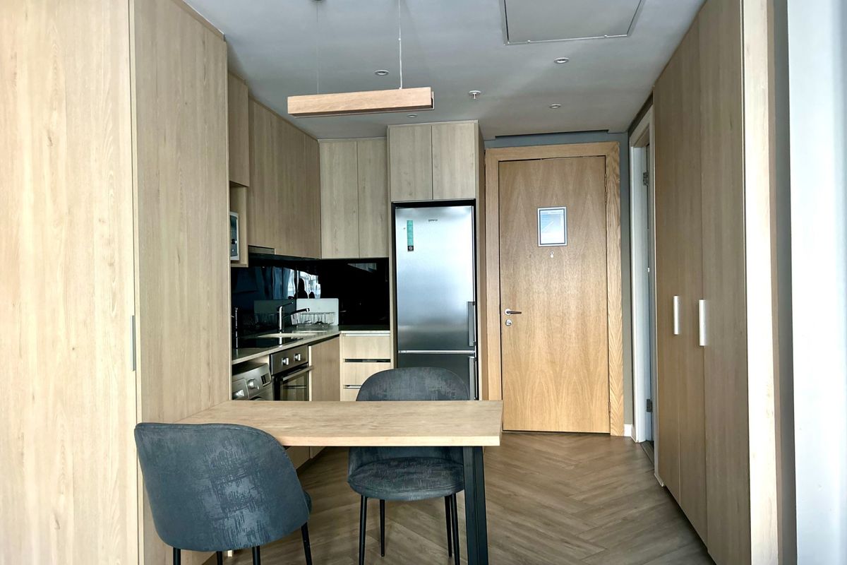 Modern kitchen featuring light wood cabinetry, integrated appliances, herringbone flooring, and a compact dining area, presenting a clean and contemporary aesthetic.