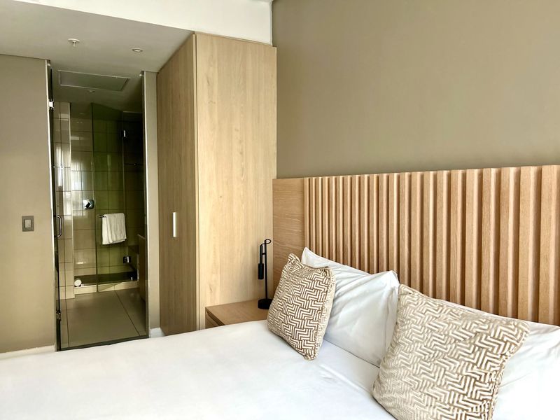 Modern bedroom featuring a custom slatted timber headboard, integrated wardrobe, and an en-suite bathroom with a glass-enclosed shower.