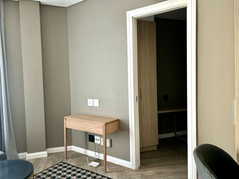 A modern bedroom featuring herringbone flooring, neutral wall tones, and a doorway leading to a walk-in closet area with built-in cabinetry.