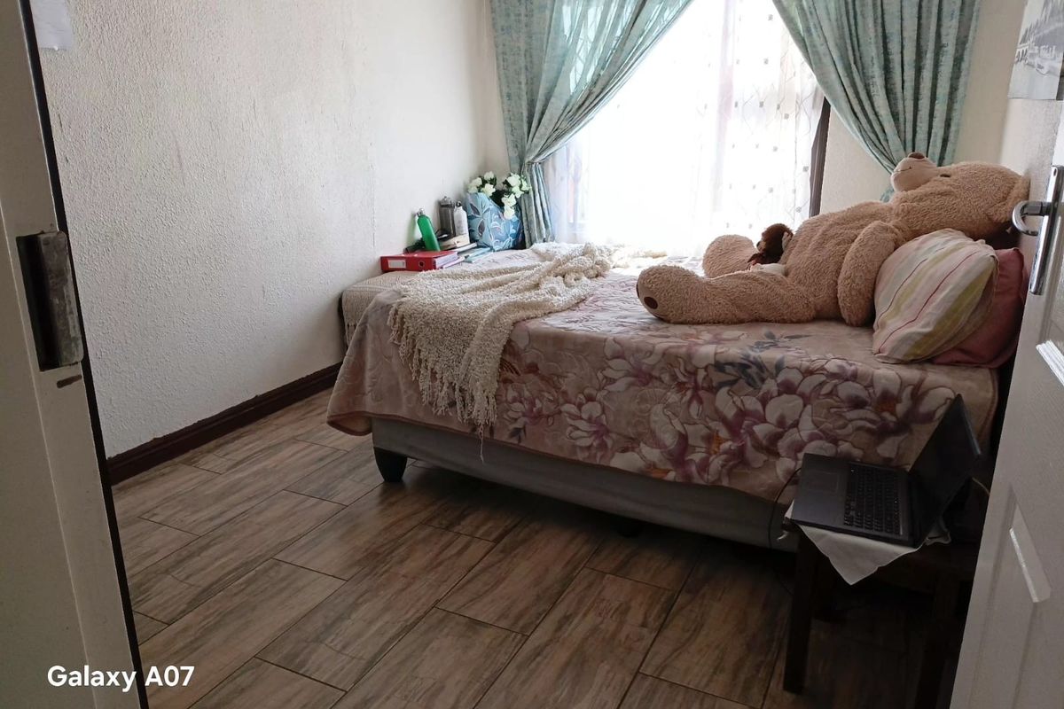 A bedroom featuring wood-look tile flooring and natural light from a window with curtains.