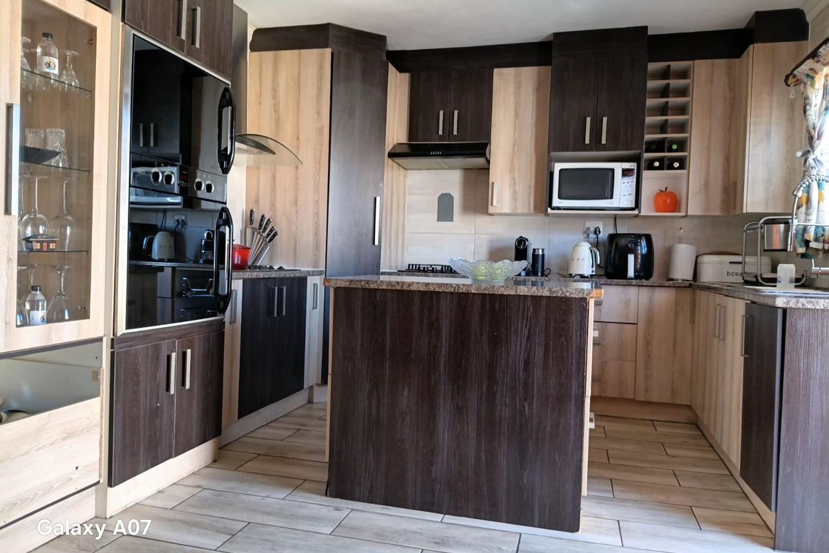 A modern kitchen featuring two-tone cabinetry, granite countertops, a central island, built-in oven, and extractor fan with tiled flooring throughout.
